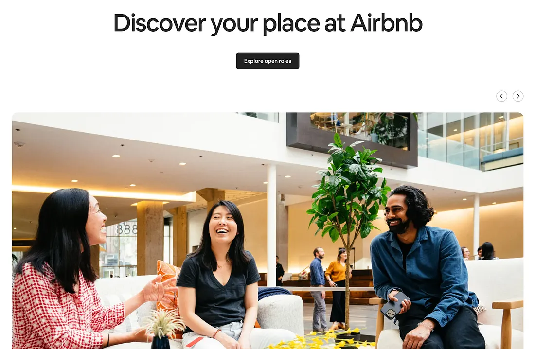 Airbnb 招募頁面截圖，標題為「Discover your place at Airbnb」，附有「Explore open roles」按鈕。下方配圖為三位員工在明亮的辦公空間內輕鬆交談，氣氛愉快。