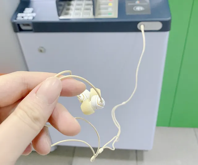 一隻手拿著插入 ATM 耳機孔的耳機，示範語音輔助功能使用情境。